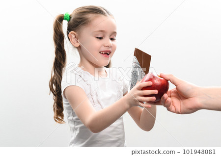 Portrait of a little girl on a white background, she chooses chocolate instead of an apple. 101948081