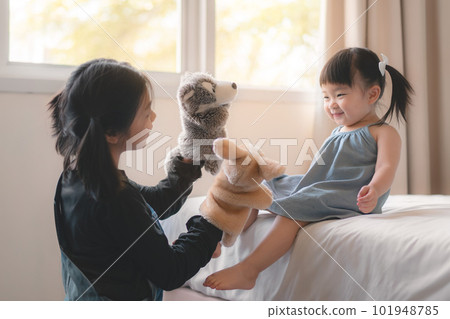 Elder asian sister and younger Asian sister playing animal hand puppet doll toys, sitting on bed, Educational preschool games, Having fun with kid at home concept.; 101948785