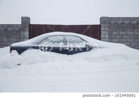 car parked near the fence is completely covered with snow car parked near the fence is completely covered with snow 101949891