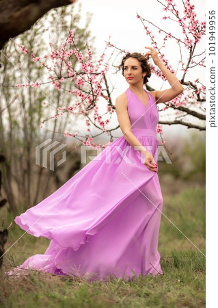 Woman peach blossom. Happy curly woman in pink dress walking in the garden of blossoming peach trees in spring 101949956