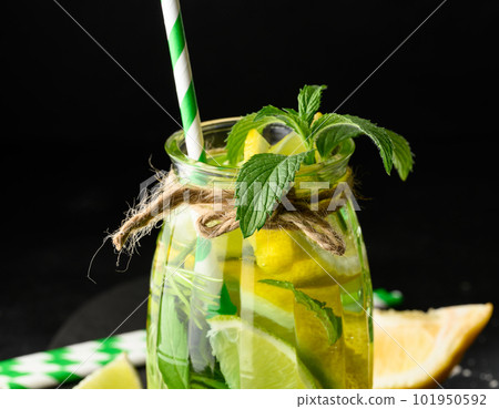 Lemonade in a transparent glass with lemon, lime, rosemary sprigs and mint leaves on a black background 101950592