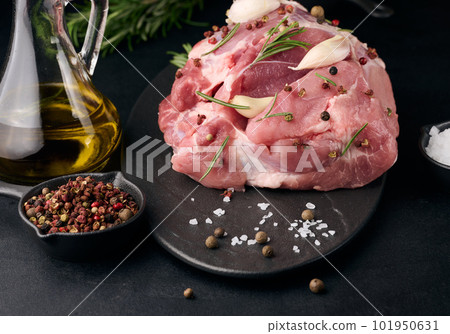 A piece of pork ham on a black board and spices olive oil, salt, rosemary branch and pepper 101950631