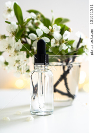 Clear glass cosmetic dropper bottle and white cherry flowers with bokeh lights, care product mockup Clear glass cosmetic dropper bottle and white cherry flowers with bokeh lights, care product mockup 101951551