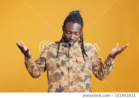 Faithful religious man standing with palms faced to sky, asking god for forgiveness in studio over yellow background. Hopeful african american religious person showing gratitude, praying to jesus 101951611