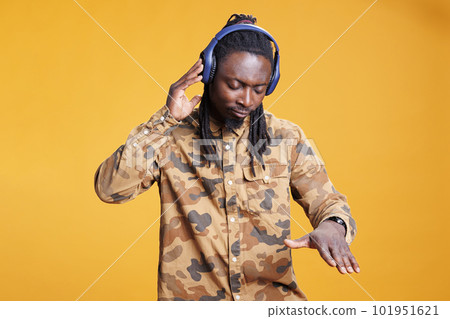 Yoyful african american man listening to favourite song, dancing and feeling happy in studio over yellow background. Smiling young adult enjoying radio music on hedset during leisure time. Yoyful african american man listening to favourite song, dancing and feeling happy in studio over yellow background. Smiling young adult enjoying radio music on hedset during leisure time. 101951621