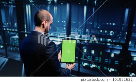 Data center technician holding tablet with green screen in server room, looking at isolated chroma key display. IT engineer inspecting mainframe computer processor, mockup template. Tripod shot. Data center technician holding tablet with green screen in server room, looking at isolated chroma key display. IT engineer inspecting mainframe computer processor, mockup template. Tripod shot. 101951622