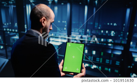 Network engineer doing system check on green screen, using tablet showing chroma key display with isolated copyspace in server room. IT technician working with cyber security. Tripod shot. Network engineer doing system check on green screen, using tablet showing chroma key display with isolated copyspace in server room. IT technician working with cyber security. Tripod shot. 101951630