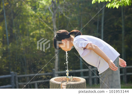 Elementary school girl drinking water in summer park Elementary school girl drinking water in summer park 101953144