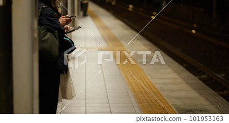 晚上，一位女士在車站站台上看著智能手機等火車 101953163