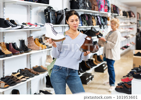 Focused asian woman chooses boots in the style of grinders Focused asian woman chooses boots in the style of grinders 101953601