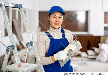 Smiling female repairer with float trowel standing indoors Smiling female repairer with float trowel standing indoors 101953692