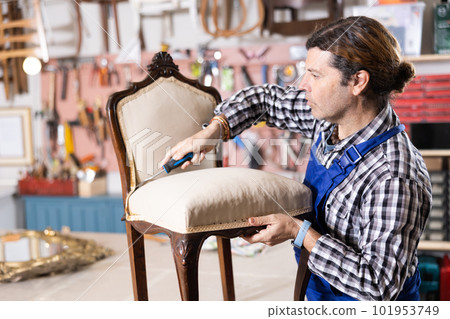 Skilled middle-aged male furniture repair specialist in uniform restoring Victorian chair during workday in workshop Skilled middle-aged male furniture repair specialist in uniform restoring Victorian chair during workday in workshop 101953749