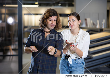 Hardware store employee showing client selection of materials on phone Hardware store employee showing client selection of materials on phone 101953834