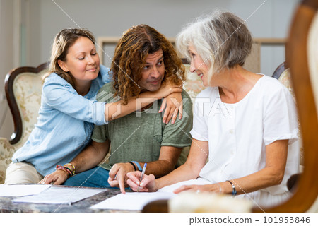 Happy couple and mature lady writing down plans on the sofa at cosy home 101953846