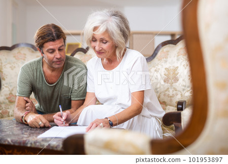 Aged woman and man sign documents sitting in room interior Aged woman and man sign documents sitting in room interior 101953897