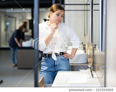 in plumbing department,thoughtful woman inspects round white ceramic sinks with faucets 101954008