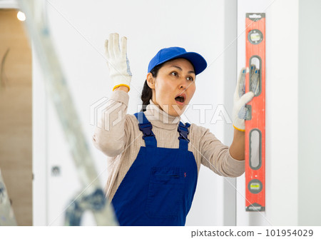 Amazed woman worker measuring wall with level 101954029