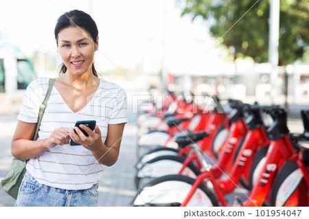 Oriental woman using smartphone near bike share station Oriental woman using smartphone near bike share station 101954047