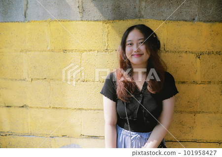 portrait of asian young woman standing against yellow wall with sunlight and shade with smiling face 101958427