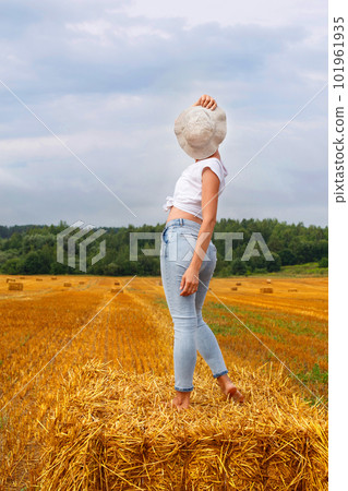 girl in straw hat stands on a haystack on a bale in the agricultural field after harvesting 101961935