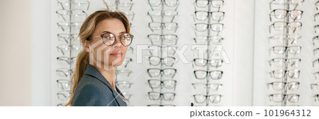 Focused Middle-aged woman in jacket trying to choose glasses in an optics store 101964312