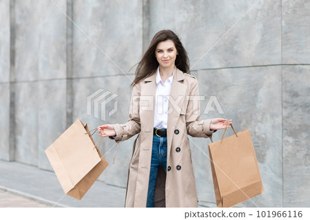 A girl in a casual clothes with shopping bags and lots of purchases near the shopping center smiling hands you her package, consumerism sale and people concept 101966116