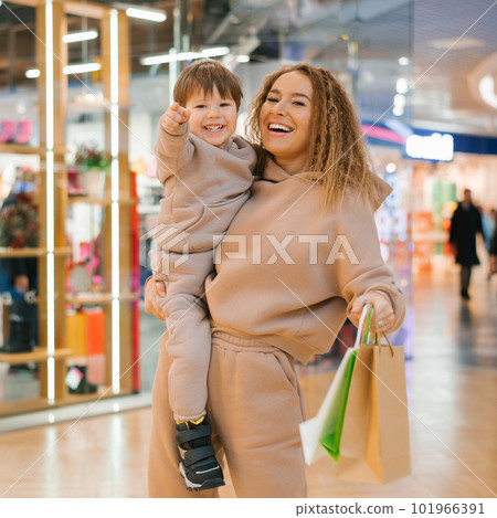 Smiling mother carries her little happy son in her arms, holds shopping bags in her hands and walks around the store on sale 101966391