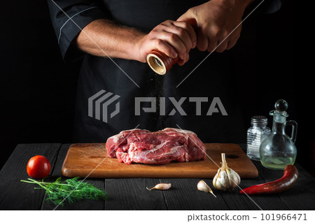 Cook cooking raw meat fillet and adding pepper or chili for marinade on black background. Working environment in kitchen in restaurant or cafe. Cook cooking raw meat fillet and adding pepper or chili for marinade on black background. Working environment in kitchen in restaurant or cafe. 101966471