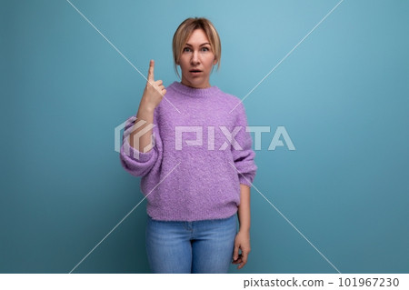 portrait of brilliant blonde young woman in lilac sweater holding thumbs up on bright background 101967230
