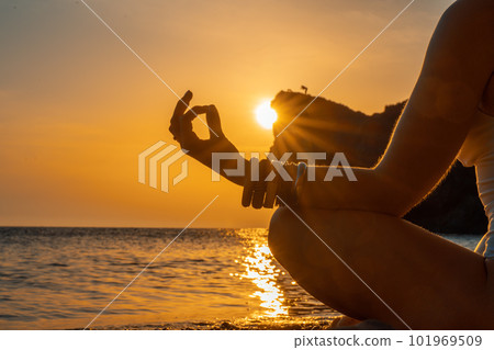 Woman tourist enjoying the sunset over the sea mountain landscape. Sits outdoors on a rock above the sea. She is wearing jeans and a blue hoodie. Healthy lifestyle, harmony and meditation Woman tourist enjoying the sunset over the sea mountain landscape. Sits outdoors on a rock above the sea. She is wearing jeans and a blue hoodie. Healthy lifestyle, harmony and meditation 101969509