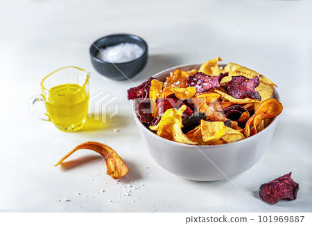 Healthy mixed vegetable chips in a bowl on light surface with marine salt and oil 101969887