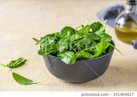 Fresh spinaches in black bowl with olive oil and grey napkin backside on light sand background 101969927