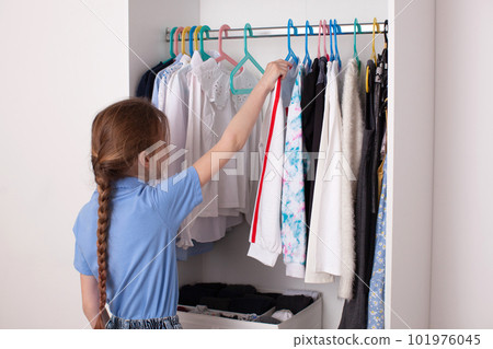 A ten-year-old girl chooses clothes in the closet. 101976045