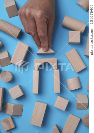 high angle view of a man building a house with some wooden building blocks on a blue background surrounded by some more building blocks 101976465