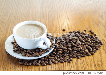 Cup of coffee in a white cup and coffee beans on wooden table background, top view. Cup of coffee in a white cup and coffee beans on wooden table background, top view. 101977584
