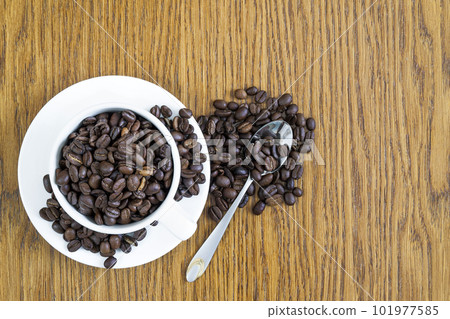 Cup of coffee in a white cup and coffee beans on wooden table background, top view. Cup of coffee in a white cup and coffee beans on wooden table background, top view. 101977585