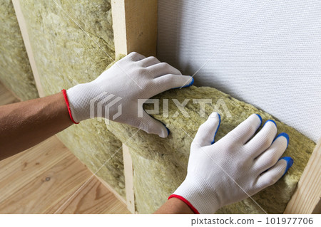 Close-up of worker hands in white gloves insulating rock wool insulation staff in wooden frame for future walls for cold barrier. Comfortable warm home, economy, construction and renovation concept. Close-up of worker hands in white gloves insulating rock wool insulation staff in wooden frame for future walls for cold barrier. Comfortable warm home, economy, construction and renovation concept. 101977706