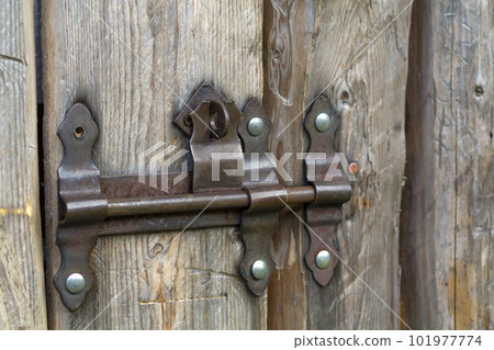Close-up of lit by sun old rough made of wooden planks house door or barn gate with iron rusty slide bolt lock. Outdated technology, safety, security and protection from thieves concept. Close-up of lit by sun old rough made of wooden planks house door or barn gate with iron rusty slide bolt lock. Outdated technology, safety, security and protection from thieves concept. 101977774