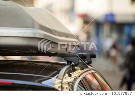 Close-up detail of light new shiny expensive modern car with roof trunk, luggage box container for long distance traveling on colorful blurred background. Transportation and vehicle design concept. Close-up detail of light new shiny expensive modern car with roof trunk, luggage box container for long distance traveling on colorful blurred background. Transportation and vehicle design concept. 101977997