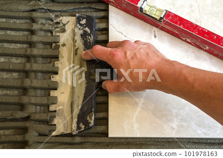 Ceramic tiles and tools for tiler. Worker hand installing floor tiles. Home improvement, renovation - ceramic tile floor adhesive, mortar, level. Ceramic tiles and tools for tiler. Worker hand installing floor tiles. Home improvement, renovation - ceramic tile floor adhesive, mortar, level. 101978163