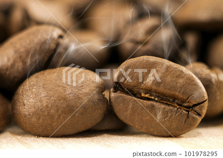 Brown coffee beans with white smoke vapour on yellow textured wooden board background close up. 101978295