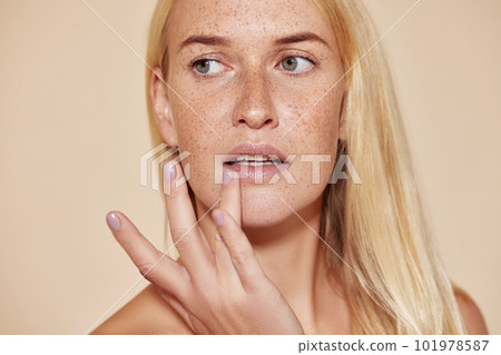 Woman with freckles touching her lip with a finger. Blond female with perfect skin applying balm on her lips. Woman with freckles touching her lip with a finger. Blond female with perfect skin applying balm on her lips. 101978587