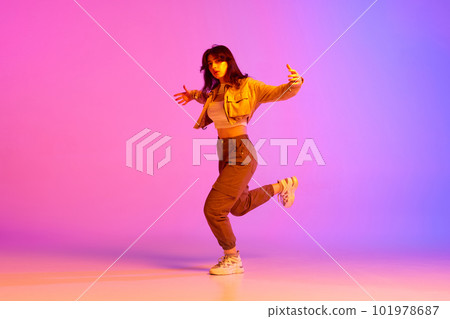 Dynamic image of young female dancer in sport style clothes dancing against gradient pink purple background in neon light 101978687