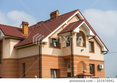 Big modern expensive luxurious residential two-stories cottage, family house with shingled brown roof, high brick chimneys, stucco walls on blue sky copy space background. Real estate selling concept. Big modern expensive luxurious residential two-stories cottage, family house with shingled brown roof, high brick chimneys, stucco walls on blue sky copy space background. Real estate selling concept. 101978842