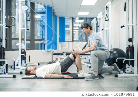 Experienced instructor assisting a man in a rehabilitation workout 101979691