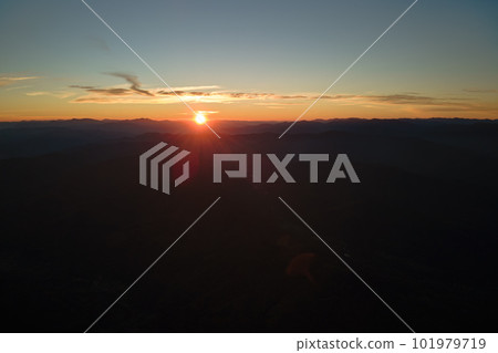 Aerial view of dark mountain hills with bright sunrays of setting sun at sunset. Hazy peaks and misty valleys in evening 101979719