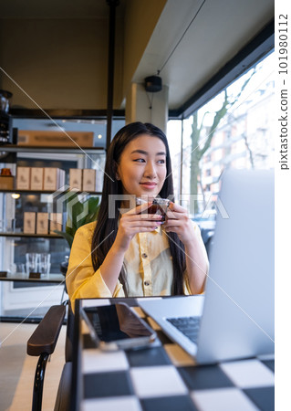 Smiling female remote employee daydreaming during the coffee break 101980112