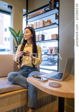 Smiling young Asian female daydreaming in a cafe 101980130