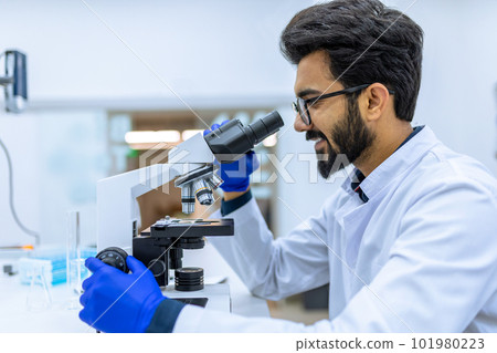 Scientist conducts experiments, adjusts specimen in petri dish and looking on it into microscope 101980223