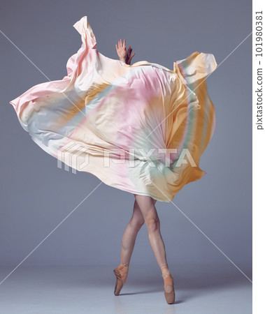 Young woman, ballerina dancing with elegance movements and fabric cover the face over grey studio background. Ballet with silk 101980381